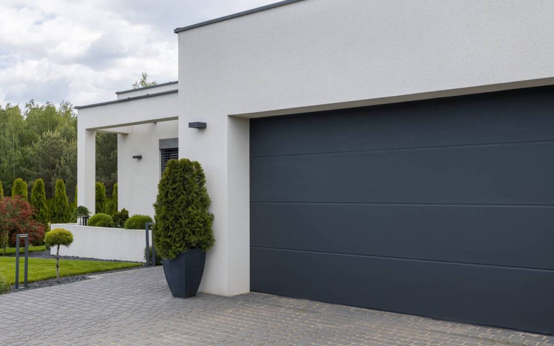Suburban home with white exterior and modern gray garage door showing greenery on left side on a cloudy but bright day.